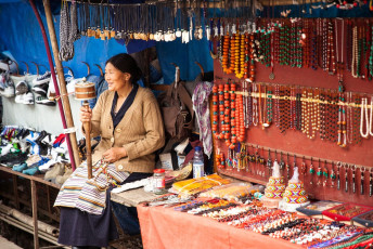 Una mujer tibetana junto a su exposición de joyas en un mercadillo de Dharamsala. En la mano sostiene una rueda de oración tradicional, Himachal Pradesh © Elena Ermakova