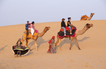 Bailarinas tradicionales vestidas con trajes típicos del Rajastán actúan para los turistas extranjeros que exploran el desierto del Thar a lomos de un camello.