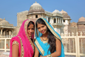 Retrato de dos hermosas mujeres jóvenes vestidas con atuendos coloridos con el Palacio Ratan Singh al fondo, ubicado dentro del fuerte Chittorgarh, RAJASTHAN ©Christophe Cappelli/ Shutterstock
