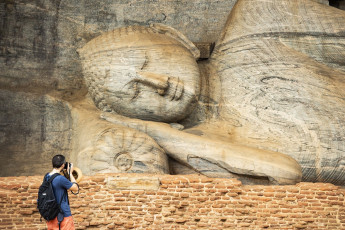 Un visitante toma una fotografía del enorme Buda reclinado, una de las cuatro estatuas talladas en roca en el Templo Gal Vihara en la antigua ciudad de Polonnaruwa cerca de Kandy In, Sri Lanka © travel wild