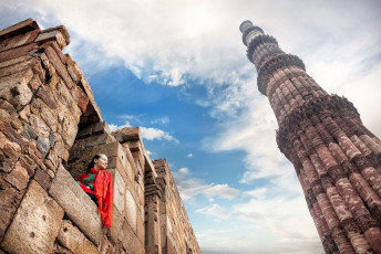 Mujer en traje rojo sentada en la ventana, mirando la torre Qutub Minar en Old Delhi, India © Pikoso.kz / Shutterstock