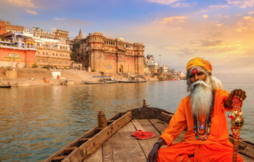 Sadhu baba en bote de madera con vista a la ciudad histórica de Varanasi y a las escaleras del río Ganges, India© Roop_Dey / Shutterstock