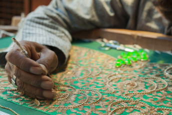 Un artesano bordando tela en el método tradicional indio usando hilo de oro, bordado zardosi de Agra - Imagen de PI