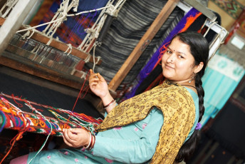 Mujer joven nepalí sonriente tejedora en telar trabajado en la fabricación de prendas de vestir y chales - Imagen de Dmitry Kalinovsky