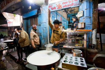 Tienda de comida rápida callejero con la persona que prepara la leche con azafrán en la Vieja Delhi - Imagen de Radiokafka