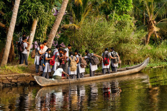Un grupo de niños de escuela abordando un barco para viajar hacia sus casas desde la escuela en la orilla de aguas tranquilas en Alappuzha, Kerala - Imagen de cornfield