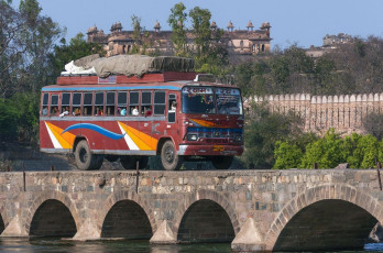 Autobús de transporte público atraviesa el puente sobre el río Betwa con el Palacio Raja en el fondo, Orchha - Claudine Van Massenhove